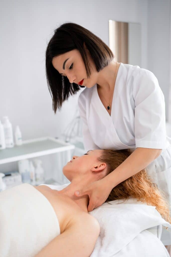 Beautician giving neck massage to woman lying on bed at beauty spa